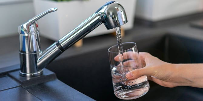 Persona llenando un vaso con agua potable del grifo de la cocina de una vivienda adecuada
